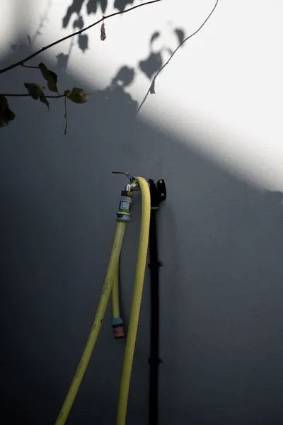 Gelber Gartenschlauch an einer Wand mit Schatten von Blättern