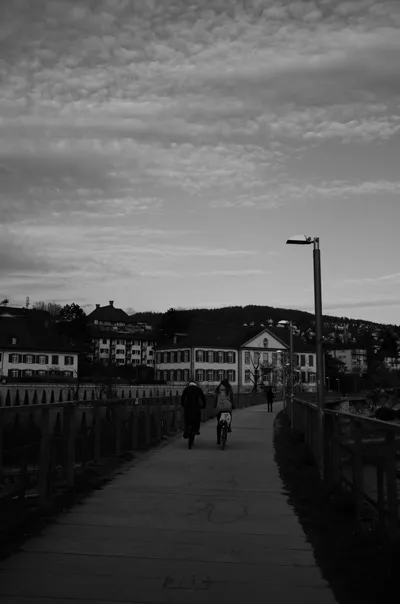 Pedestrians on a bridge under cloudy sky in black and white